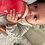 baby, bottle, hand, face, eyes, clothing, bed, blanket, person, infant, sleepwear, skin, mouth, nail, holding, cute, young, child, newborn, resting