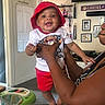 Charles Smith joined the competition — help win amazing prizes! baby, child, smile, red_hat, red_shorts, adult_hand, indoor, living_room, wall_decal, lakers_sign, family_photos, pacifier, joyful, person, holding, furniture, door, ceiling_fan, clothing, portrait