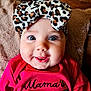 baby, child, infant, headband, leopard_print, pink_clothing, smile, face, cheeks, eyes, cute, portrait, indoors, blanket, soft_texture, apparel, bow, happy, person, closeup
