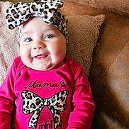 Ember joined the competition — help win amazing prizes! baby, smiling, leopard_print, headband, pink_clothing, couch, pillow, indoors, cute, happy, child, infant, apparel, pattern, portrait, person, soft_fabric, cozy, young_child, face