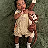 Aaron joined the competition — help win amazing prizes! baby, child, plush_toy, monkey, green_carpet, overalls, socks, curly_hair, indoor, cute, toddler, clothing, soft_toy, lying_down, expression, person, infant, hand, footwear, playful