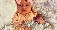 Elodie joined the competition — help win amazing prizes! baby, infant, blanket, headband, pink_bow, soft_texture, wooden_background, cozy, cute, portrait, clothing, sleepwear, child, face, hands, indoor, comfort, warm, newborn, resting