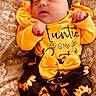 baby, newborn, sleeping, headband, yellow_clothing, sunflower_pattern, blanket, infant, cute, cozy, soft_texture, child, portrait, resting, peaceful, clothing, patterned_fabric, indoors, small_hands, toddler