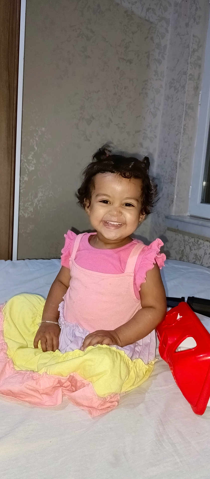 Azra Altıntaş a rejoint le concours — aidez-le/la à gagner de superbes lots ! bed, child, cute, dress, girl, happy, indoor, person, pigtails, pink, playful, portrait, red_toy, sitting, smiling, toddler, toy, wall, window, yellow