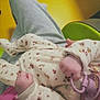 baby, hand, pacifier, clothing, onesie, floral_pattern, infant, pink, yellow_floor, gray_pants, person, closeup, casual, indoor, soft_lighting, cozy, child, cute, newborn, relaxed