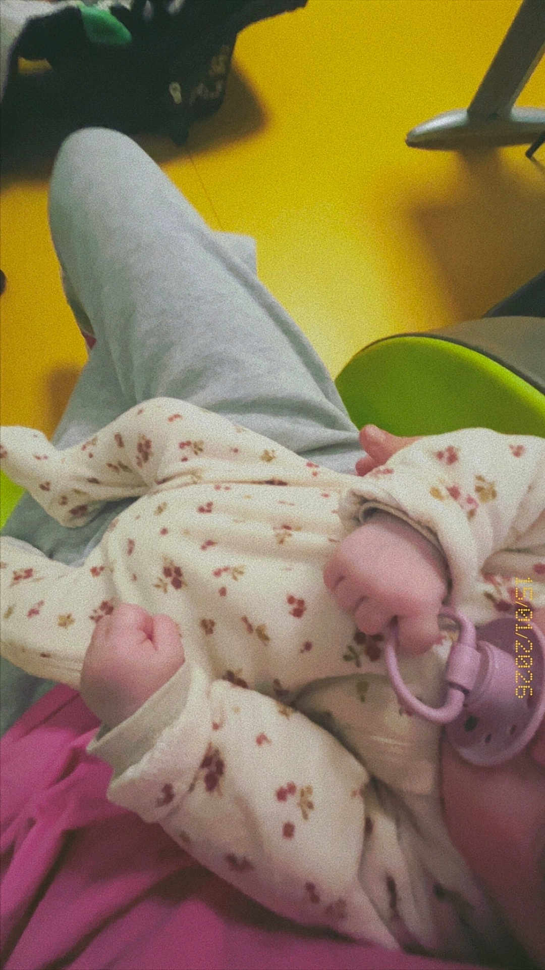 Ilyana participe au concours pour gagner de l'argent avec cette photo : baby, hand, pacifier, clothing, onesie, floral_pattern, infant, pink, yellow_floor, gray_pants, person, closeup, casual, indoor, soft_lighting, cozy, child, cute, newborn, relaxed