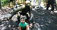 Rodrigo joined the competition — help win amazing prizes! baby, child, gorilla_statue, outdoor, people, green_clothing, shade, ground, nature, park, tourist, statue, curious, sitting, shorts, footwear, fence, backpack, sunlight, photography