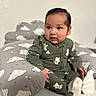Rodrigo is registered to the contest to win money with this photo: baby, child, infant, green_onesie, cloud_pattern, cushion, soft_toy, indoor, cute, smile, face, sitting, cozy, clothing, footwear, pajamas, person, portrait, young_child, curious