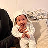 Rodrigo is registered to the contest to win money with this photo: baby, child, smiling, white_onesie, hood, cute, indoor, couch, blanket, hand, person, happy, infant, cozy, apparel, portrait, sitting, warm, soft, home