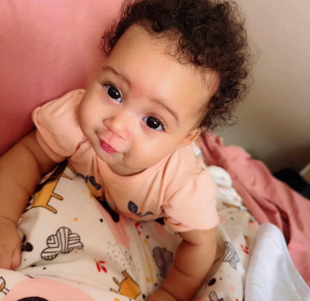 Maria participe au concours pour gagner de l'argent avec cette photo : baby, child, curly_hair, blanket, crawling, cute, indoor, person, infant, pink, patterned_blanket, face, expression, toddler, soft_lighting, clothing, skin, close_up, smile, young_child