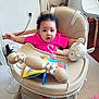 baby, high_chair, pink_shirt, curly_hair, plush_toy, stuffed_animal, book, indoor, carpet, wooden_floor, furniture, child, person, expression, toy, face, seat, cord, surprise, room