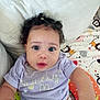 baby, infant, child, curly_hair, purple_shirt, couch, blanket, patterned_blanket, indoors, portrait, face, wide_eyes, cute, toddler, sitting, cozy, curious, skin, person, young_child
