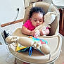 baby, high_chair, stuffed_animal, toy, cloth_book, indoor, carpet, curly_hair, pink_shirt, child, seat, focus, play, hand, face, furniture, floor, cord, table, cuddling