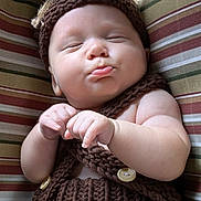 Maxim is registered to the contest to win money with this photo: baby, sleeping, pout, knitted_clothing, brown, cushion, striped, infant, peaceful, soft_skin, cute, hand, button, portrait, indoors, closeup, resting, child, newborn, cozy