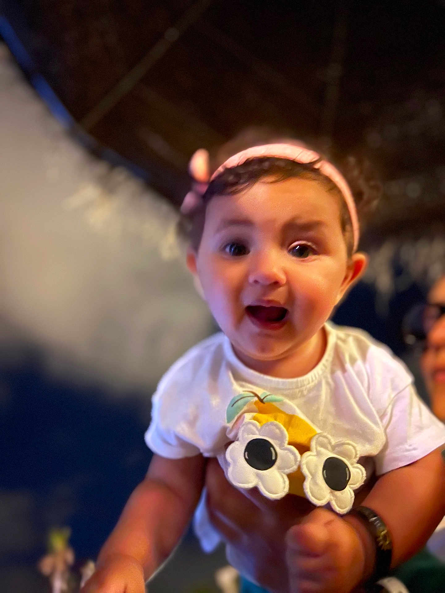 Miral a rejoint le concours — aidez-le/la à gagner de superbes lots ! baby, child, headband, white_shirt, flower_design, happy, smiling, person, cute, closeup, indoor, hand, adult_hand, night, blurred_background, portrait, young_child, bright_eyes, cheerful, casual_clothing