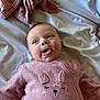 baby, infant, pink_outfit, tongue_out, bed, blanket, sleepwear, cute, expression, face, person, child, soft_texture, cozy, indoor, lying_down, playful, newborn, comfortable, fabric