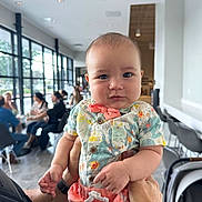 Ezra is registered to the contest to win money with this photo: baby, infant, child, person, holding, indoor, cafe, clothing, colorful, bow_tie, shorts, face, expression, cheeks, hands, people, windows, chairs, table, modern