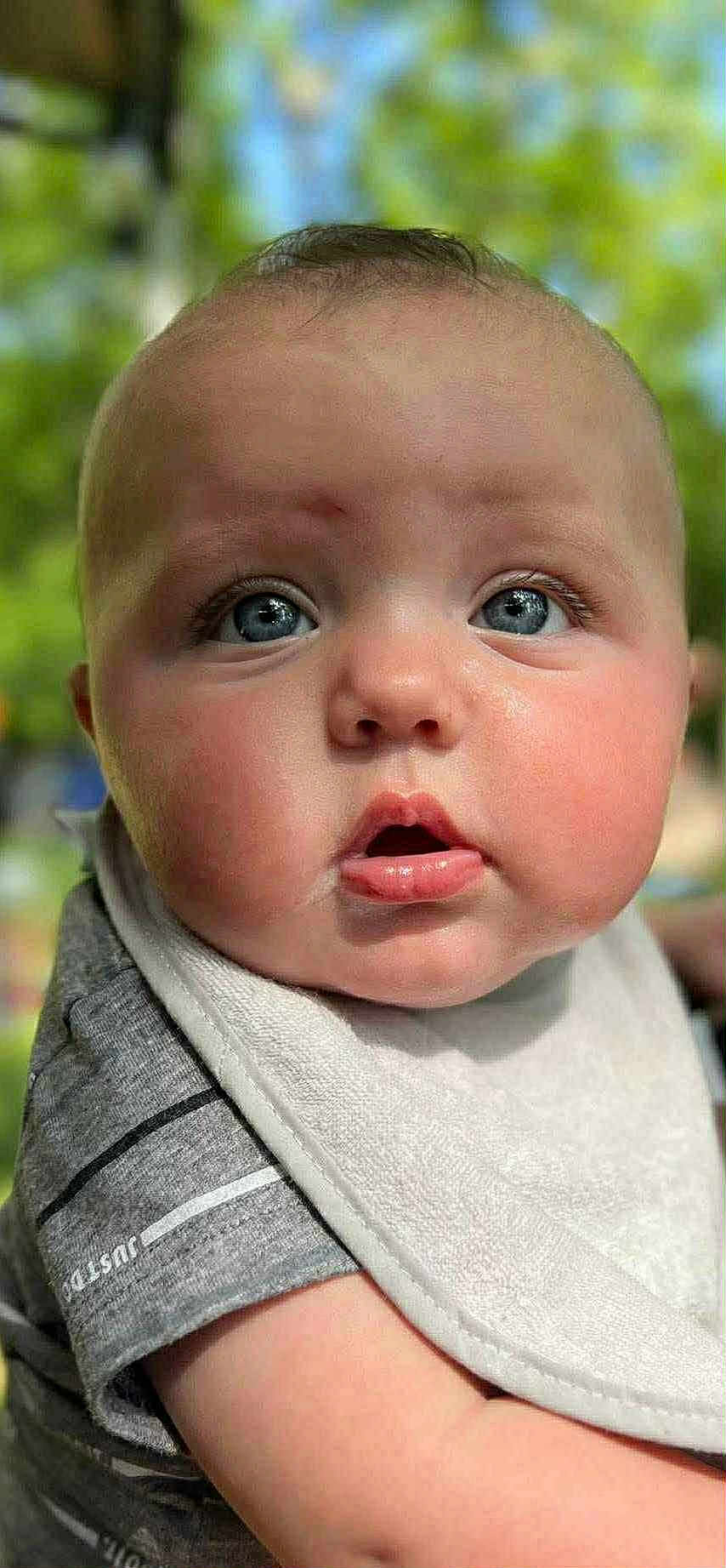 Axl Byrd joined the competition — help win amazing prizes! baby, close_up, face, blue_eyes, bib, chubby_cheeks, expression, outdoor, greenery, soft_focus, infant, cute, portrait, child, apparel, striped_shirt, skin, person, head, young