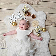 Thaïs participe au concours pour gagner de l'argent avec cette photo : baby, infant, smiling, white_dress, headband, bow, christmas, ornaments, gifts, wooden_floor, fluffy_rug, festive, holiday, decorations, noel_sign, cute, lying_down, celebration, child, portrait