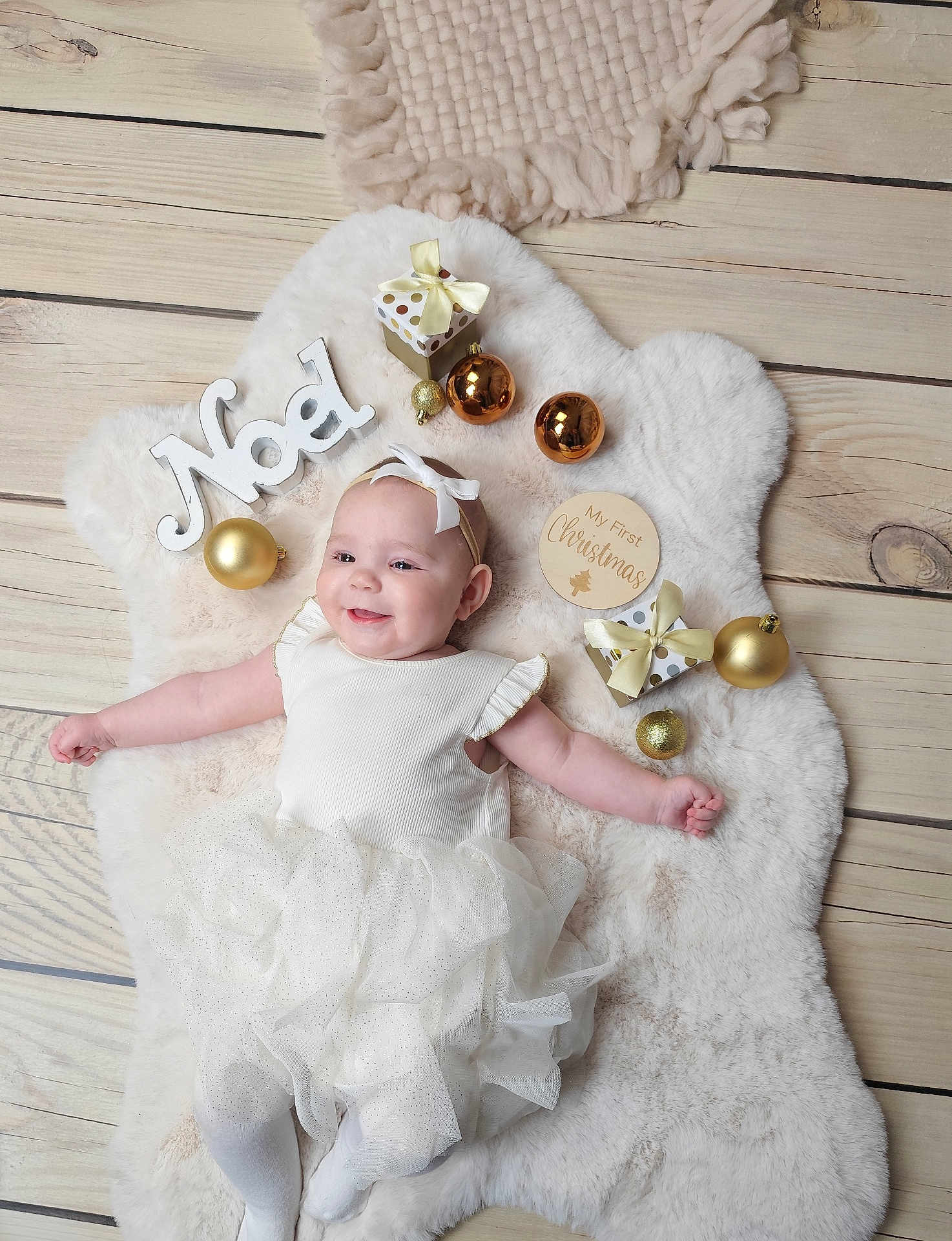 Thaïs participe au concours pour gagner de l'argent avec cette photo : baby, infant, smiling, white_dress, headband, bow, christmas, ornaments, gifts, wooden_floor, fluffy_rug, festive, holiday, decorations, noel_sign, cute, lying_down, celebration, child, portrait