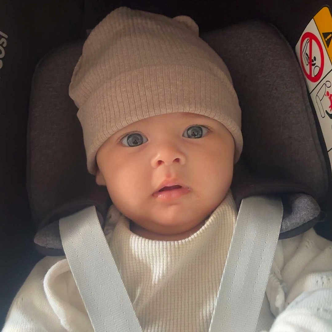 Mencia participe au concours pour gagner de l'argent avec cette photo : baby, car_seat, child, child_seat, close_up, curious, cute, face, hat, indoor, infant, portrait, seat, seatbelt, soft_light, straps, sweater, warm_clothing, wide_eyes, young_child