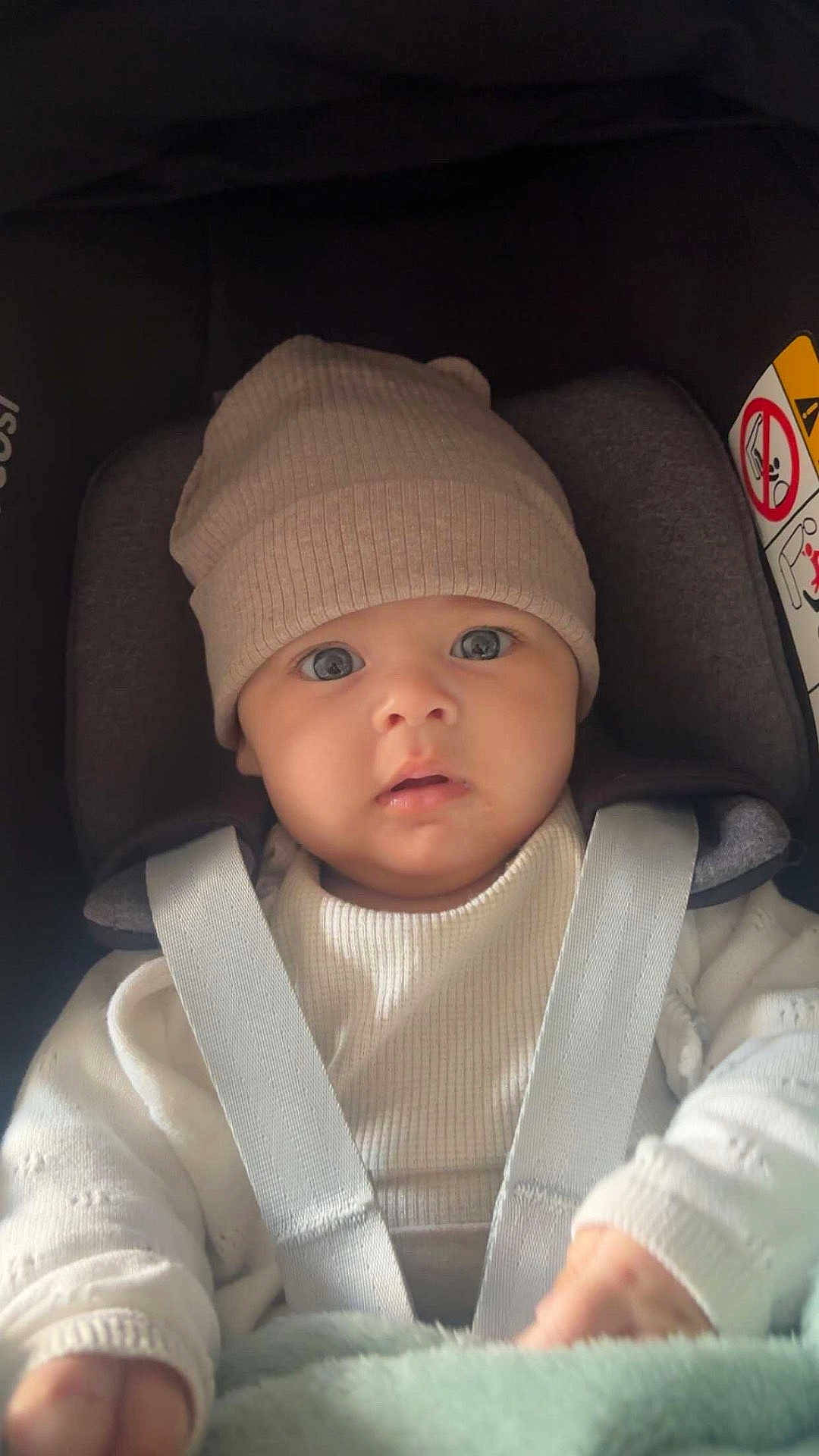 Mencia participe au concours pour gagner de l'argent avec cette photo : baby, infant, car_seat, hat, sweater, child, straps, seatbelt, wide_eyes, curious, indoor, cute, portrait, close_up, warm_clothing, seat, child_seat, soft_light, young_child, face