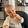 adult_male_on_tv, baby, candid, chewing, child, closeup, cute, expression, face, furniture, high_chair, home, indoor, infant, kitchen, person, sitting, spoon, television, white_clothing