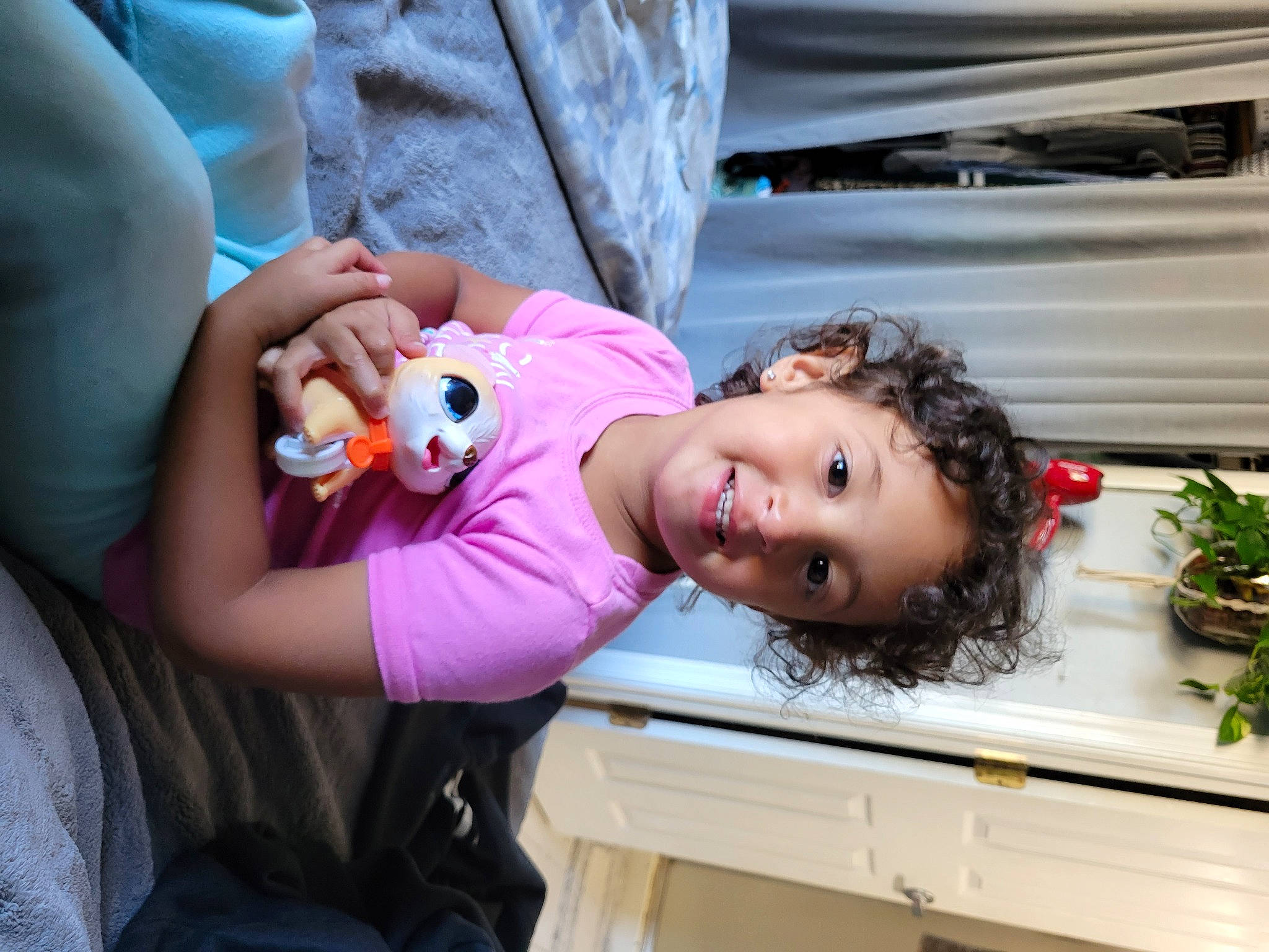 Emilia is registered to the contest to win money with this photo: baby, child, dress, eyelash, facial_expression, flowerpot, fun, happy, joy, leisure, lip, mouth, nail, person, plant, room, skin, smile, stuffed_toy, toddler