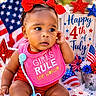 baby, child, red_bows, pink_bib, girls_rule_text, 4th_of_july_sign, american_flag, patriotic_decorations, flowers, stars, red_clothing, curly_hair, sitting, face, portrait, celebration, holiday, cute, independence_day, colorful