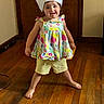 child, toddler, chef_hat, paper_hat, floral_dress, shorts, standing, smiling, indoors, wooden_floor, wooden_door, portrait, full_body, playful, costume, kitchen_theme, home, barefoot, happy, photography