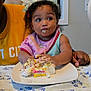toddler, child, cake, birthday_cake, messy, food, tablecloth, plate, pink_bib, headband, adult_hand, indoor, celebration, happy, eating, person, young_child, curly_hair, colorful, party