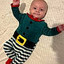 Isaac a rejoint le concours — aidez-le/la à gagner de superbes lots ! baby, child, smile, face, person, infant, clothing, costume, holiday, striped_pants, red_booties, green_top, belt_design, blanket, lying_down, hand_raised, cute, happy, indoor, portrait