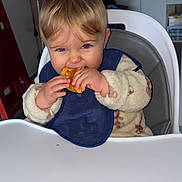 Isaac a rejoint le concours — aidez-le/la à gagner de superbes lots ! toddler, child, high_chair, bib, pastry, food, eating, indoor, fleece_jacket, blonde_hair, face, hands, kitchen, window, cabinet, chair, table, person, baby, cute