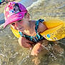 child, beach, water, swimsuit, floaties, pink_cap, splashing, sunny, summer, outdoor, playful, happy, young, cartoon_hat, vacation, holiday, fun, sand, waves, nature