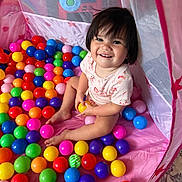 Alina joined the competition — help win amazing prizes! toddler, child, play_tent, plastic_balls, colorful, smiling, happy, indoor, toy, playtime, pink, purple, yellow, green, blue, red, orange, person, short_hair, casual_clothing