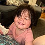 toddler, child, smiling, baby_bottle, indoor, living_room, couch, pink_shirt, happy, face, person, hair, skin, arm, patterned_clothing, carpet, furniture, home, cute, playful