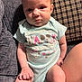 baby, infant, onesie, clothing, sitting, couch, pillow, face, skin, hand, leg, cute, expression, indoors, person, child, young, happy, text_on_clothing, fabric