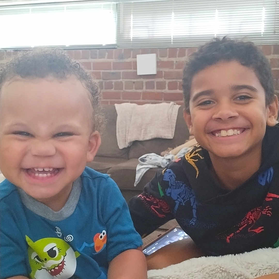 Akeem joined the competition — help win amazing prizes! baby, bodypart, brick, clothing, couch, face, finger, furniture, hand, happy, head, laughing, mouth, person, photography, portrait, sitting, smile, t_shirt, teeth