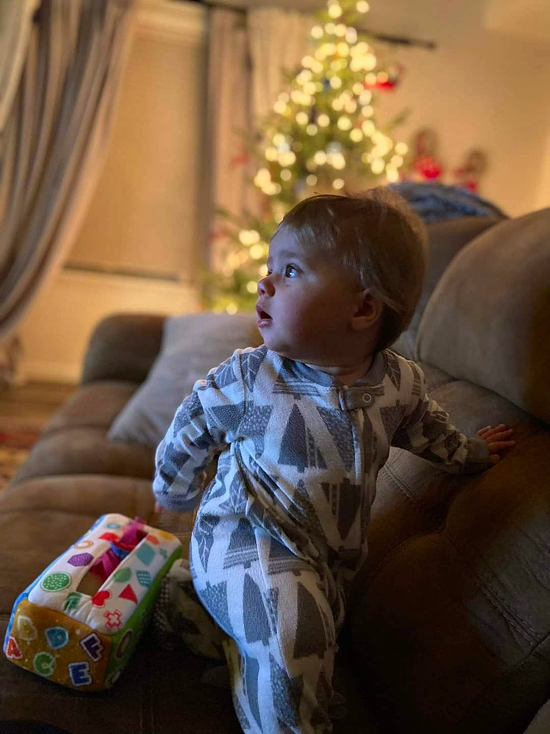 Charli joined the competition — help win amazing prizes! child, christmas, christmas_decoration, christmas_ornament, christmas_tree, comfort, couch, curtain, event, fun, hairstyle, happy, head, holiday, lap, living_room, person, sitting, toddler, tree