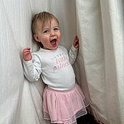 Adahlia joined the competition — help win amazing prizes! toddler, child, girl, smiling, happy, standing, clothing, pink_skirt, tutu, white_shirt, curtains, indoor, floor, sock, long_sleeve, portrait, cute, fun, expression, small_person