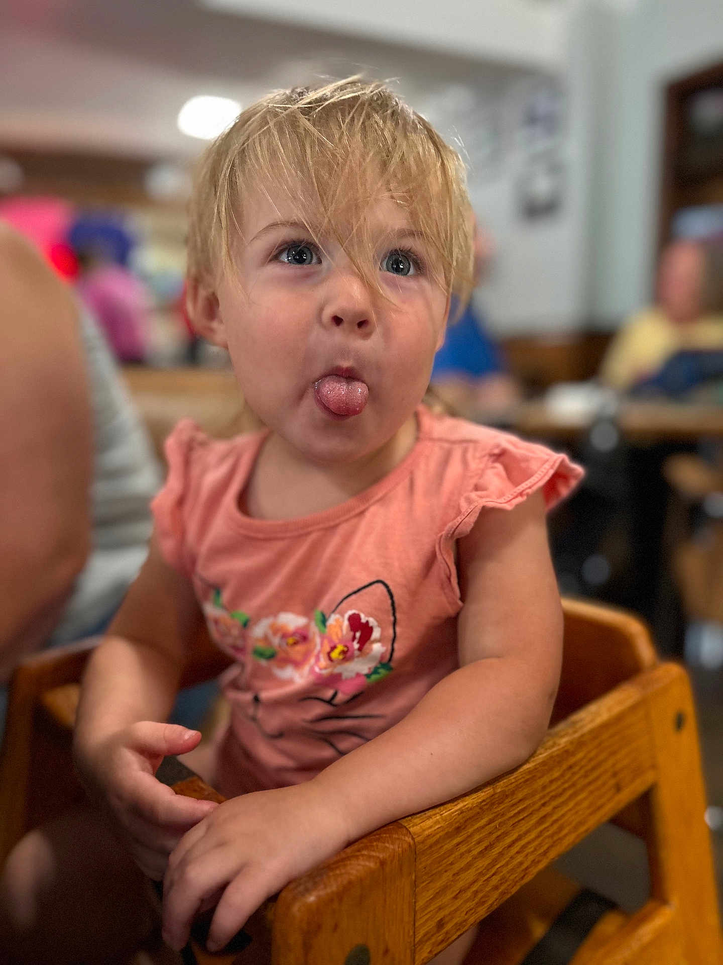 Adahlia is registered to the contest to win money with this photo: blonde_hair, blue_eyes, casual_clothing, child, cute, expression, family, floral_design, funny_face, indoor, person, pink_shirt, playful, portrait, seat, smile, toddler, tongue_out, wooden_high_chair, young_child