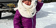 Adahlia is registered to the contest to win money with this photo: toddler, child, snow, winter_clothing, purple_snowsuit, white_hood, booties, outdoor, vehicle, license_plate, snowy_ground, waving, cold_weather, smiling, face, person, daylight, happy, nature, cute