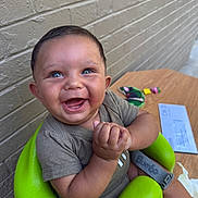 Deangelo joined the competition — help win amazing prizes! baby, child, smiling, happy, blue_eyes, green_seat, clapping_hands, short_sleeve_shirt, brick_wall, wooden_table, toys, letter, indoor, person, infant, cute, seat, joyful, portrait, clothing