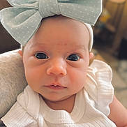 Marlow is registered to the contest to win money with this photo: baby, child, infant, headband, bow, white_clothing, strawberry_patch, closeup, portrait, face, eyes, cute, soft_light, indoors, blurred_background, person, newborn, gaze, holding, small_hand