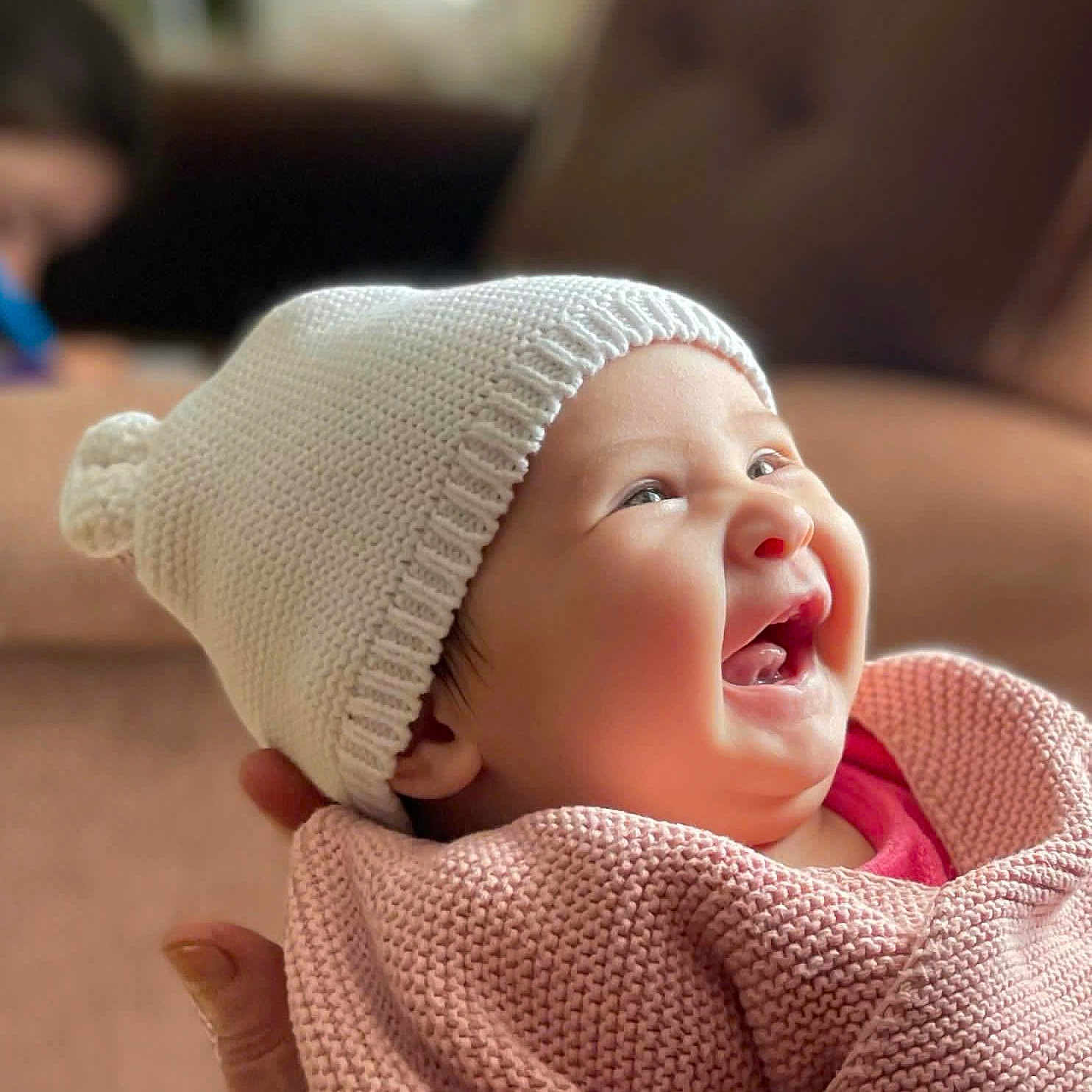 Privat Emma a rejoint le concours — aidez-le/la à gagner de superbes lots ! apparel, baby, background_blur, blanket, child, closeup, cozy, cute, face, hand, happy, indoor, infant, knit_hat, person, portrait, sitting, smiling, soft_light, warm