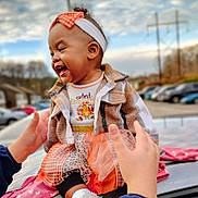 Kailani is registered to the contest to win money with this photo: baby, child, smiling, outdoor, headband, plaid_jacket, tutu_skirt, car, parking_lot, hands, cloudy_sky, cute, fall_fashion, happy, person, footwear, sitting, supporting_hands, jacket, toddler