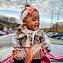 Kailani joined the competition — help win amazing prizes! toddler, child, smiling, plaid_jacket, headband, skirt, slippers, blanket, car_roof, outdoor, parking_lot, cloudy_sky, happy, cute, portrait, fashion, warm_clothing, baby, sitting, daytime