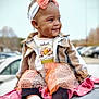 Kailani is registered to the contest to win money with this photo: toddler, child, smile, headband, outdoor, car, jacket, dress, happy, footwear, parked_cars, cute, fashion, person, portrait, sitting, baby, warm_clothing, playful, daytime