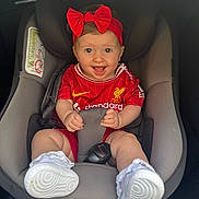 Raya joined the competition — help win amazing prizes! baby, car_seat, red_headband, red_bow, football_jersey, liverpool_jersey, smiling, happy, child, infant, white_shoes, lacy_socks, car_interior, seat_belt, sitting, cute, portrait, baby_clothing, child_in_car, safety