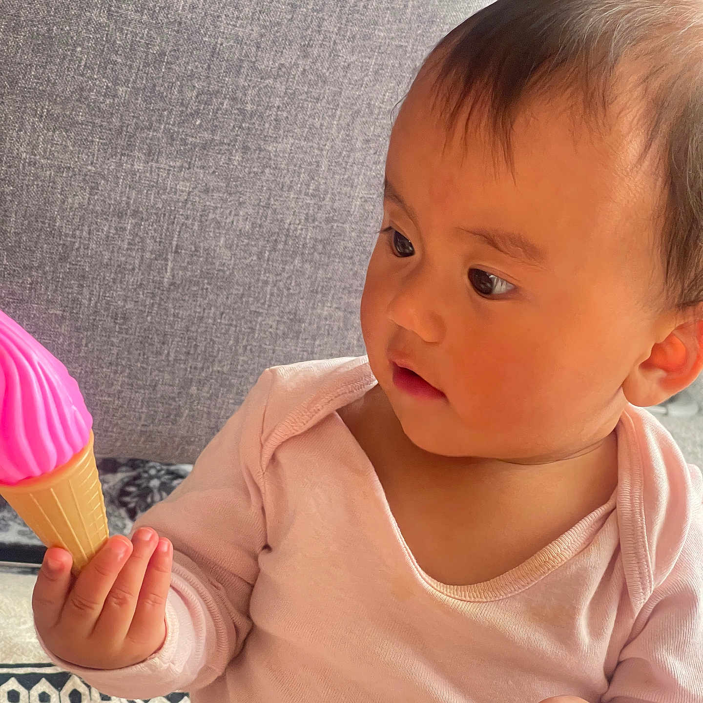 Viona joined the competition — help win amazing prizes! baby, child, clothing, couch, curious, cute, exploring, face, hand, ice_cream_cone, indoors, infant, looking, patterned_blanket, pink, portrait, sitting, soft_lighting, toy, young